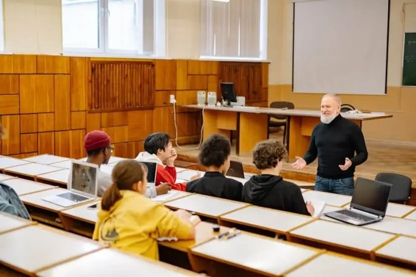 A teacher explaining the conjugation and usage of the German verb 'haben' to students in a lecture hall.