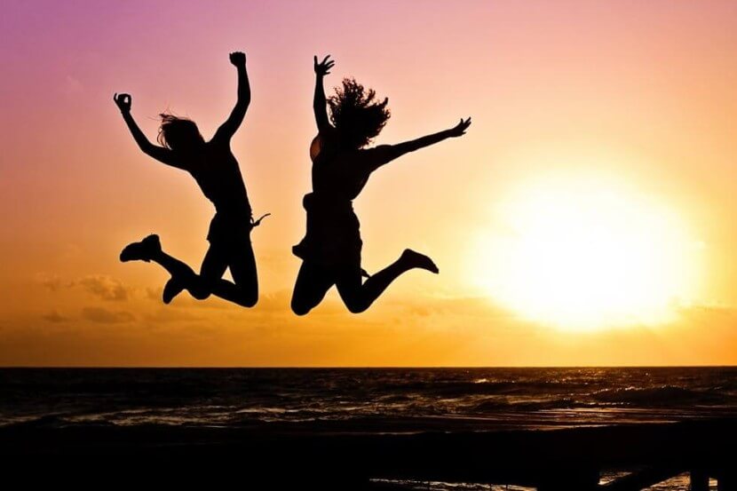 Two friends jumping with joy at sunrise, representing excitement and happiness using German adjectives and verbs for emotions and feelings.