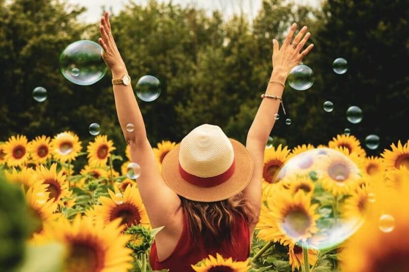 Woman celebrating in a sunflower field surrounded by bubbles while learning German nouns vocabulary for emotions and feelings.