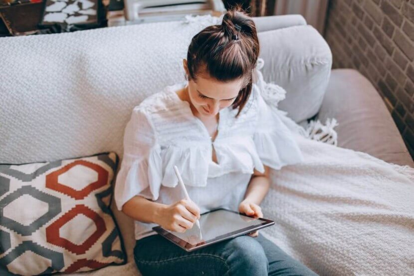 A woman learning German dative vs accusative cases, writing notes on a tablet while sitting on a couch.