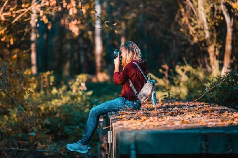 Woman sitting on a wooden platform taking photographs in a natural setting, illustrating German hobbies vocabulary for photography.