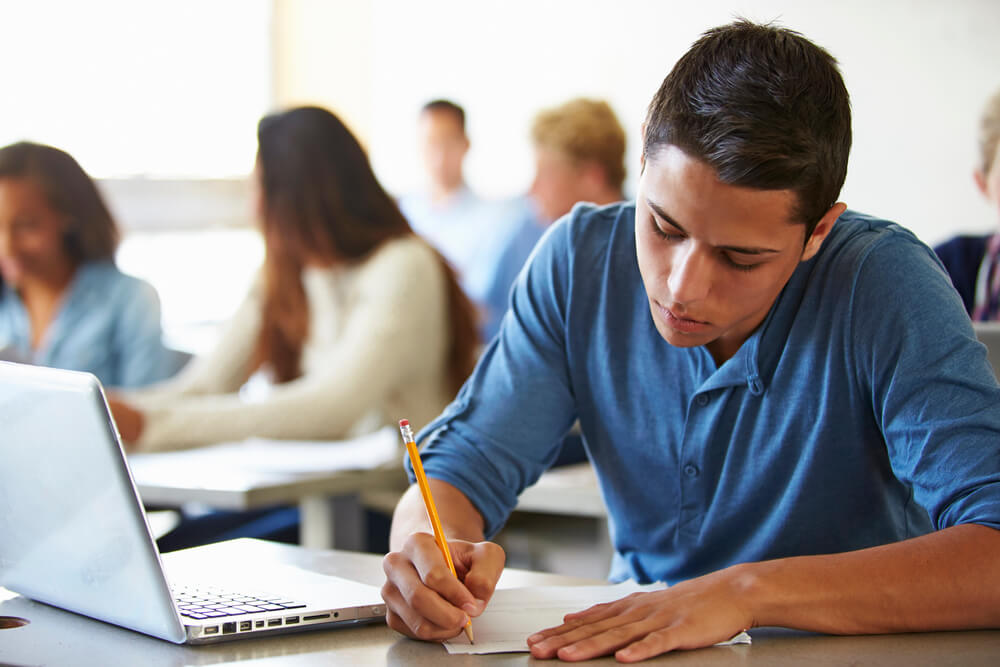 Male student studying German grammar on dass vs das in a classroom with a laptop and notebook.