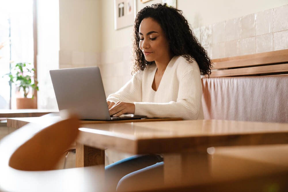 Woman studying German weak (regular) verbs on a laptop in a cozy café setting.