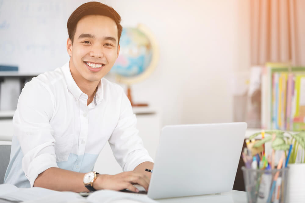 Smiling man learning German relative clauses with prepositions on a laptop in a bright office.