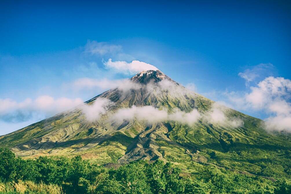 Active volcano with green slopes and smoke rising from the peak, an example for geography vocabulary in German.