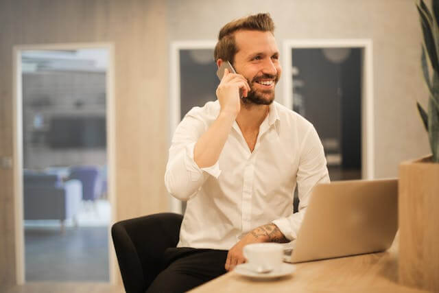 Smiling man in an office talking on the phone, representing professional phone conversations in German.