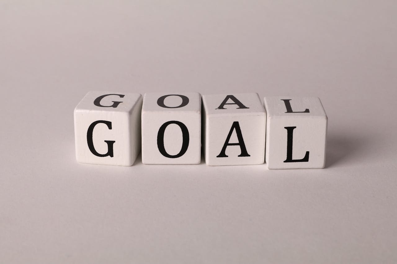 Four white cubes spelling out the word 'GOAL' are neatly aligned on a smooth surface, symbolizing the clarity and focus needed to achieve das Ziel (the goal) in any project or career path.