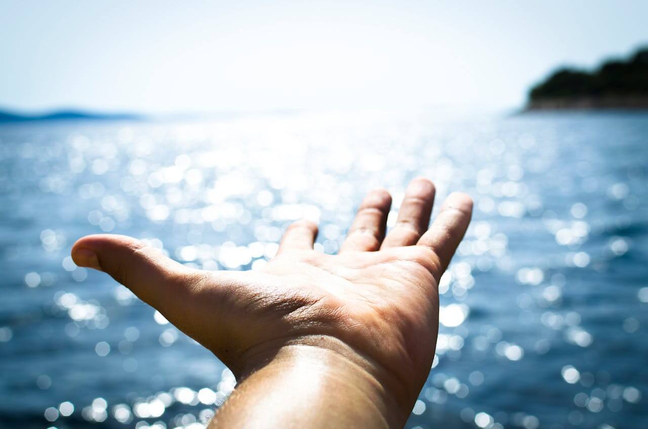 An open human hand reaching out towards sparkling blue water, clearly showing the fingers. This image is featured in our German vocabulary lesson on the masculine noun der Finger.
