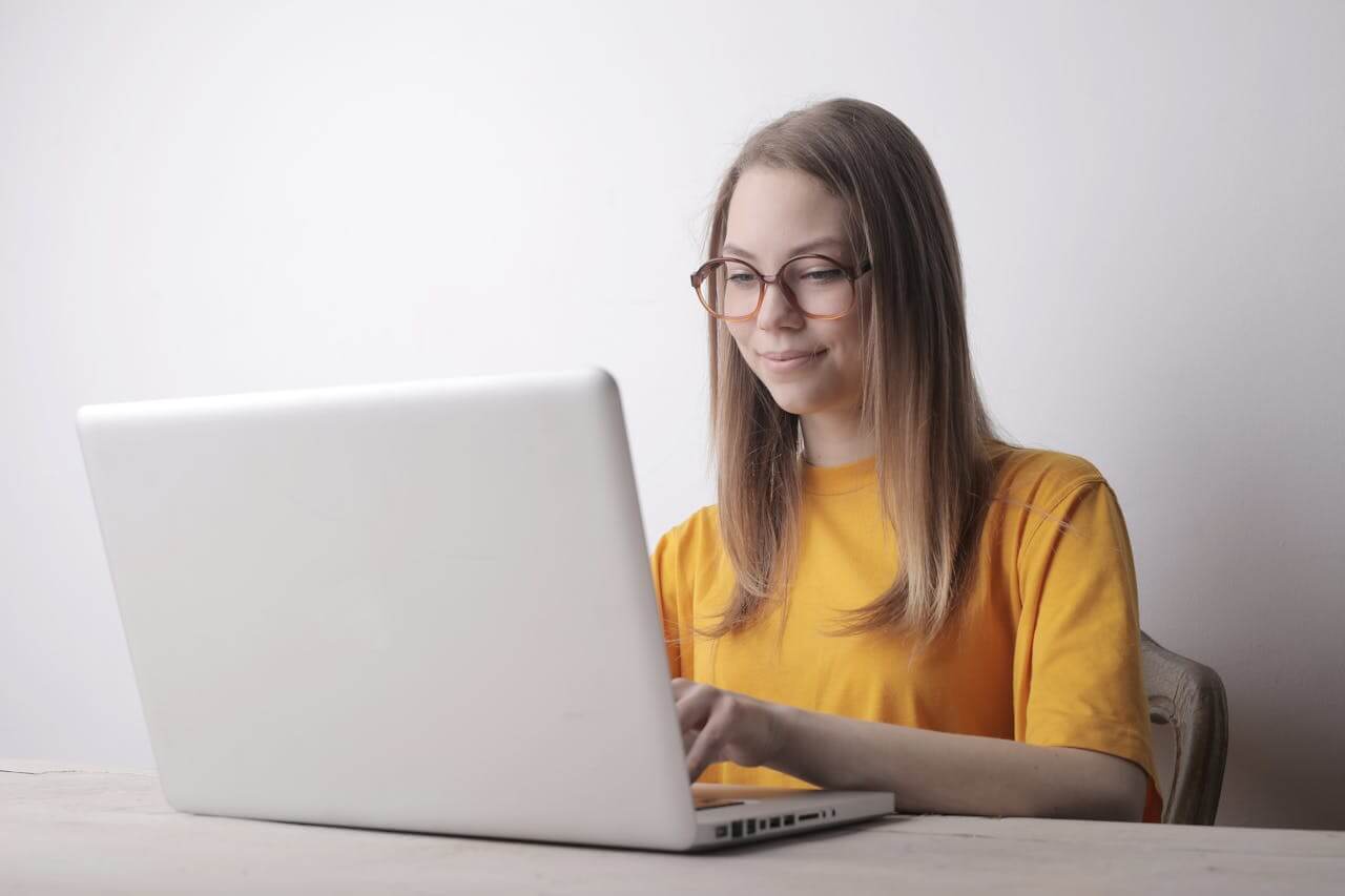 A young woman sits at a laptop and writes die Bewerbung (the job application), focusing on her documents while typing at home.