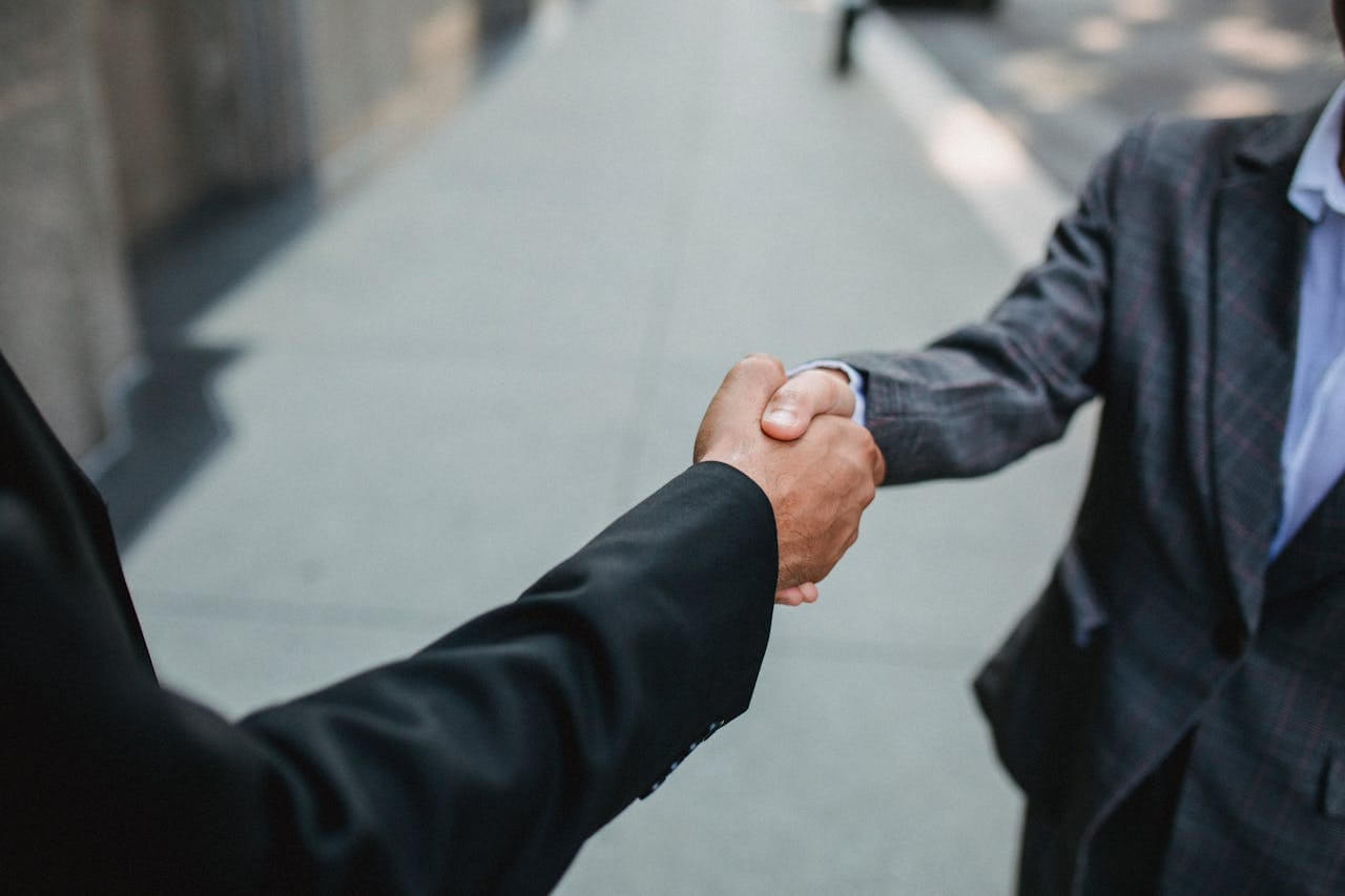 Two professionals in business suits shake hands on a city walkway, symbolizing the successful agreement reached at the end of die Verhandlung (the negotiation).