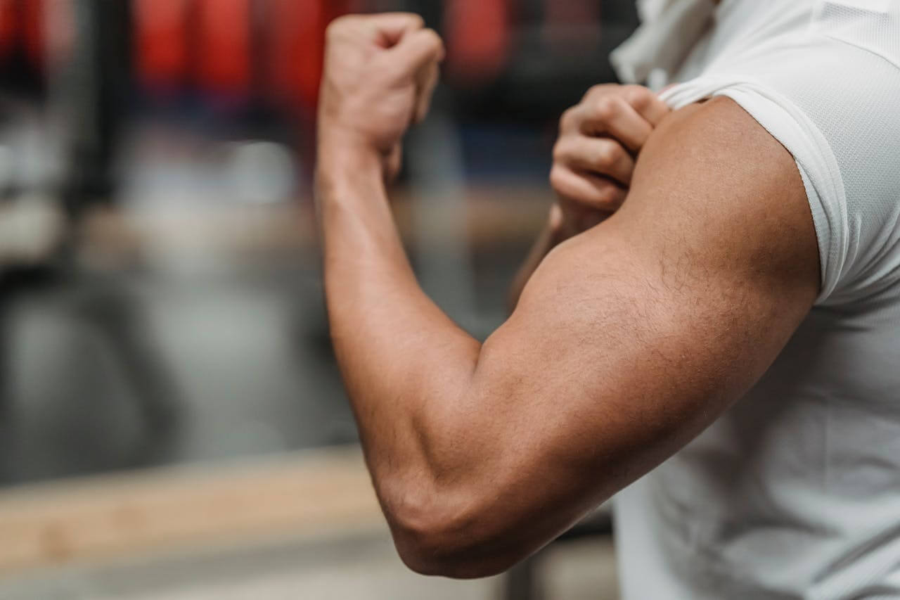 Close-up of a person flexing their bicep muscle in a gym, illustrating the German masculine noun "der Muskel".