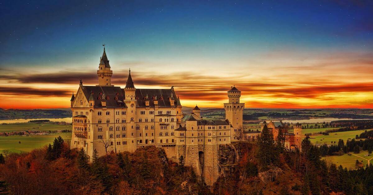 The iconic Neuschwanstein Castle in Bavaria, Germany, during a vibrant sunset surrounded by autumn trees, serving as the hero image for the grammar guide on the German noun 'der Onkel'.