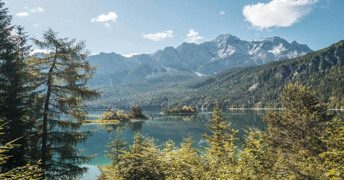 Breathtaking view of the alpine Eibsee lake with small islands and the massive snow-capped Zugspitze mountain range in Germany, serving as the hero image for the grammar guide on the German noun 'die Familie'.