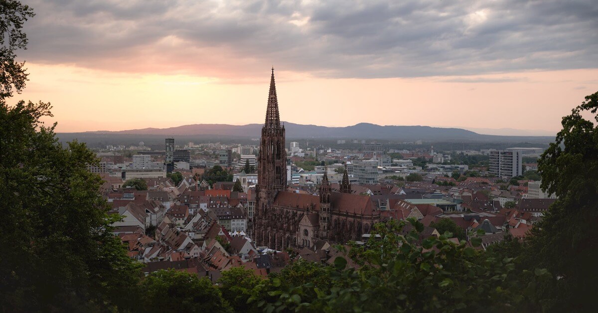 High-angle view of the Freiburg Minster cathedral with its iconic spire rising above the historic city center at sunset, serving as the hero image for the grammar guide on the German noun 'die Tante'.