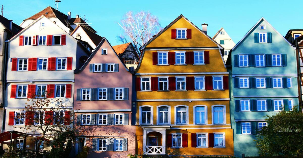 Row of colorful, traditional German timber-framed houses with red shutters under a blue sky, serving as the hero image for the grammar guide on the German noun 'die Tochter'.