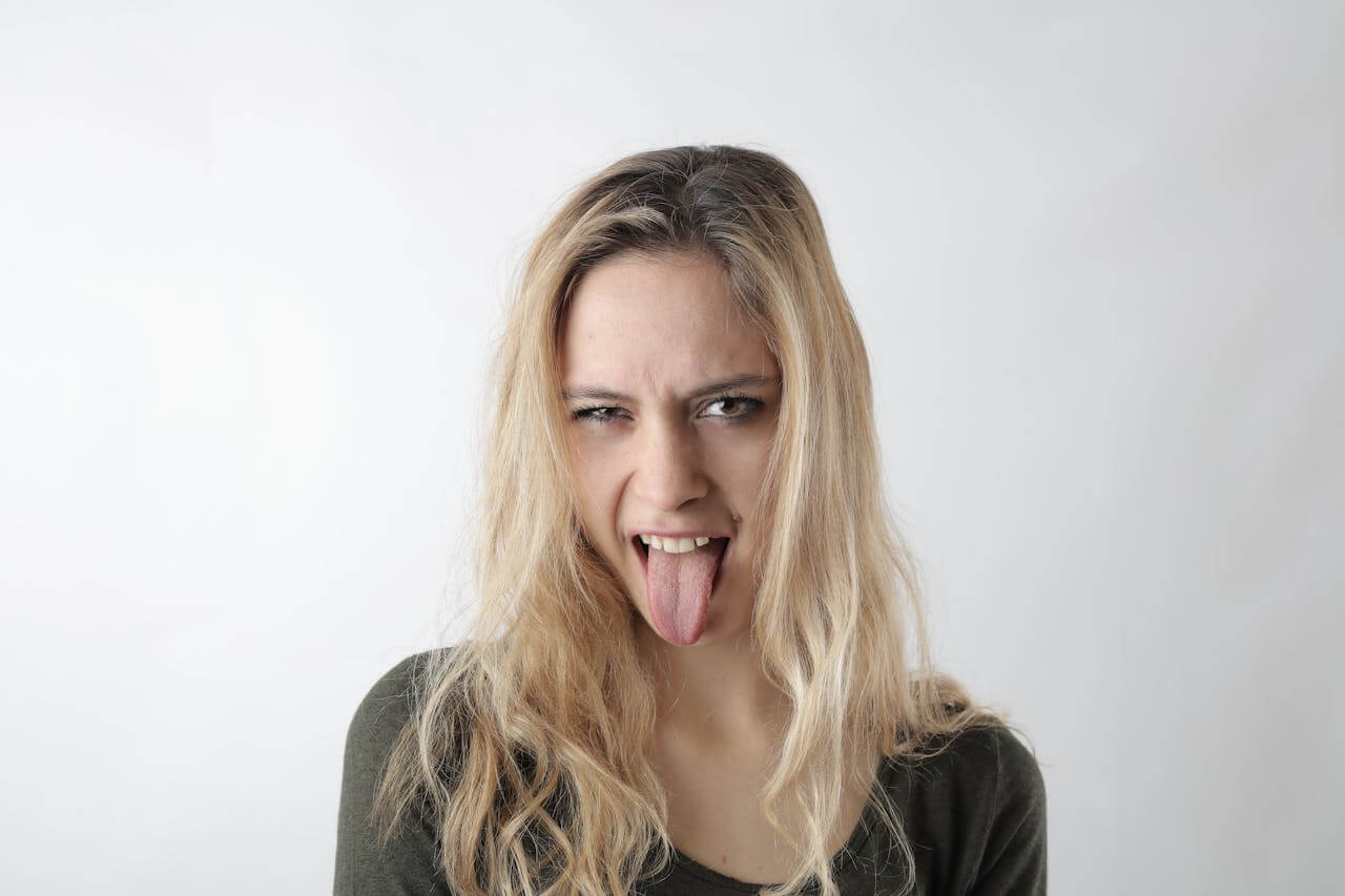 A young woman sticking her tongue out at the camera, illustrating the German feminine noun "die Zunge".