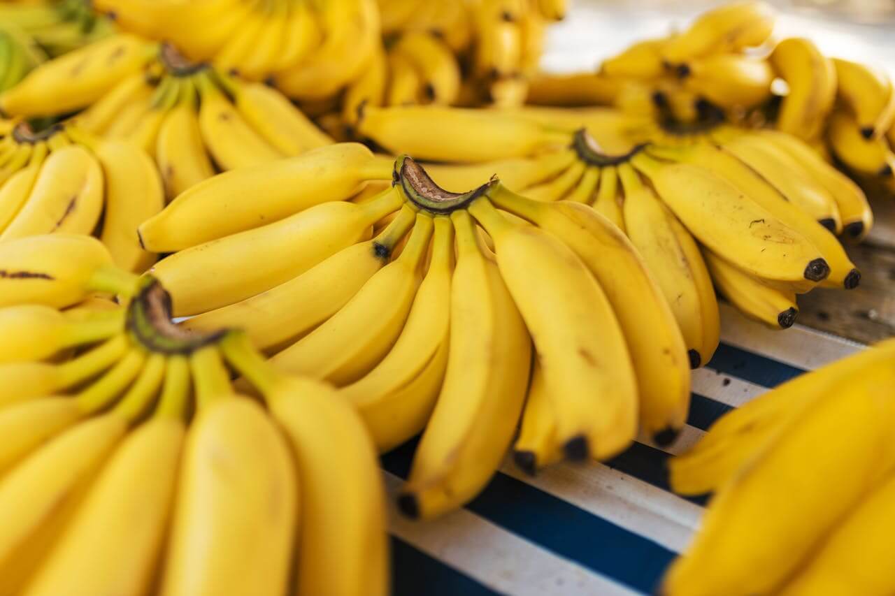 Several bunches of ripe, bright yellow fruit are neatly arranged on a striped market display, highlighting die Banane (the banana), which serves as a sweet and healthy tropical fruit perfect for a quick energy boost.
