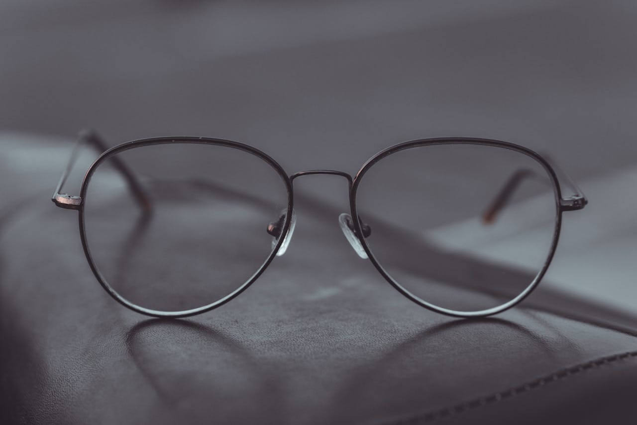 A pair of elegant, thin-framed metal spectacles rests on a dark leather surface, showcasing die Brille (the glasses) which is used to correct vision and provide clarity for the wearer.
